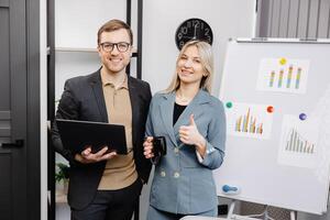 Business people with laptop discussing new projects in office. A young woman and a man stand near flipcharts and solve work issues photo