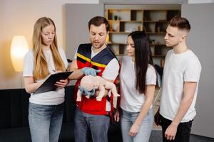 Group of people learning how to make first aid with dummy child during the training indoors photo