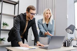 Concentrated male businessman looking at computer monitor, working with a young female worker on a project, people holding a meeting with a client or interviewing a job candidate. photo