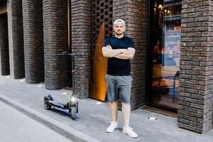 Young handsome man in n white baseball cap and casual clothies standing near electric scooter on the street. photo