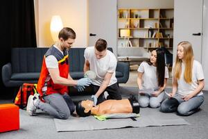 Young man instructor helping to make first aid heart compressions with dummy during the group training indoors photo