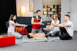 Young man instructor helping to make first aid heart compressions with dummy during the group training indoors photo