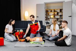 Young man instructor helping to make first aid heart compressions with dummy during the group training indoors photo