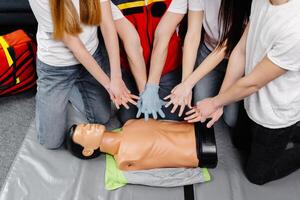 Young man instructor helping to make first aid heart compressions with dummy during the group training indoors photo