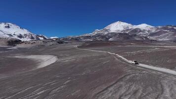 A white SUV drives through a stark desert landscape with snowcapped mountains in the background video