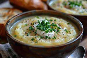 A bowl of creamy leek and potato soup, garnished with chives and a swirl of cream, served with a crusty bread roll. photo