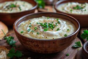 A bowl of creamy leek and potato soup, garnished with chives and a swirl of cream, served with a crusty bread roll. photo