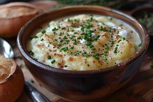 A bowl of creamy leek and potato soup, garnished with chives and a swirl of cream, served with a crusty bread roll. photo