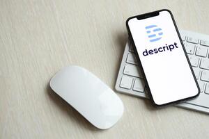 KYIV, UKRAINE - MARCH 17, 2024 Descript logo on iPhone display screen with apple keyboard and mouse on table photo