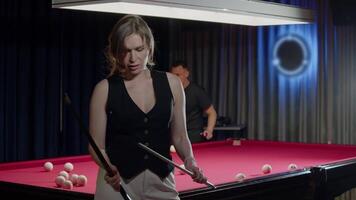 Woman is disassembling a cue at the end of a game, standing in front of an unusual red pool table in a nightclub. Mid shot. Slow motion video