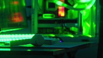 fechar-se tiro do fones de ouvido e uma teclado deitado em uma hacker mesa, com néon verde iluminação piscando dentro a fundo. fechar acima. lento movimento. video