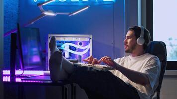 Man is relaxed while working at his powerful, expensive, beautiful gaming computer with neon lighting, with his feet up on the table. Medium shot. Slow motion. video