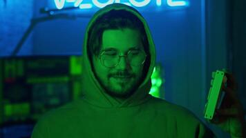 Portrait of a programmer is looking directly into the camera, illuminated by neon lights. He lifts the keyboard in front of him and begins to press the keys. Close up. Slow motion. video
