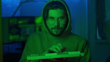 Portrait of a hacker, wearing a hoodie, typing something on a keyboard, and looking directly into the camera. Close up. Slow motion. video