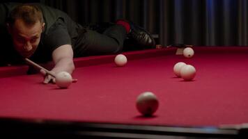 Billiards player lies down on the table to aim at the ball. With an accurate and powerful stroke, he successfully pockets the ball. Mid shot. Slow motion video