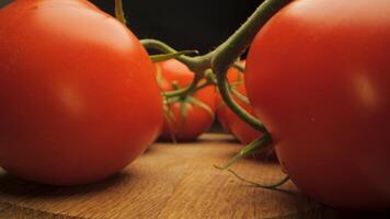 A close-up view of red ripe tomatoes sitting on a wooden cutting board. The tomatoes are still attached to their stems, showing the green leaves and the vibrant red color of the fruits. video