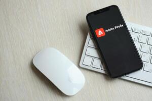 KYIV, UKRAINE - MARCH 17, 2024 Adobe Firefly logo on iPhone display screen with apple keyboard and mouse on table photo