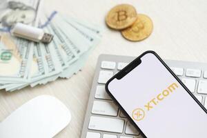 KYIV, UKRAINE - MARCH 15, 2024 XTcom logo on iPhone display screen on white keyboard with money and bitcoins photo