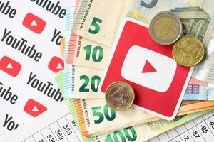 KYIV, UKRAINE - APRIL 20, 2024 YouTube logo and many euro money bills. Symbol of famous social network platform and european currency banknotes photo