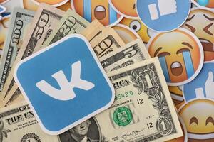 KYIV, UKRAINE - APRIL 20, 2024 VK logo and many usd money bills. Symbol of famous social network platform and dollar currency banknotes on lot of emoji reactions photo