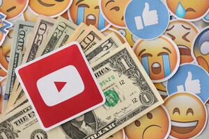 KYIV, UKRAINE - APRIL 20, 2024 YouTube logo and many usd money bills. Symbol of famous social network platform and dollar currency banknotes on lot of emoji reactions photo