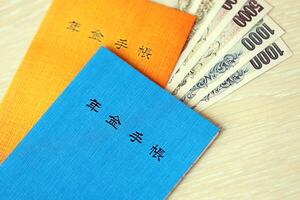 Japanese pension insurance booklets on table with yen money bills. Blue and orange books photo
