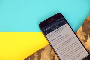 KYIV, UKRAINE - 4 MAY, 2023 Ukr Net ukrainian news portal on smartphone screen with ukrainian flag and camouflage fabric photo