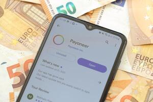TERNOPIL, UKRAINE - AUGUST 3, 2023 Payoneer application on screen on modern smartphone and many bills of euro currency photo