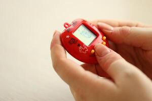 KYIV, UKRAINE - MARCH 9, 2024 Retro pet keychain game tamagotchi in red plastic case in female hands photo