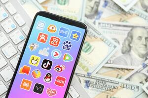KYIV, UKRAINE - APRIL 1, 2024 Asian apps icon on smartphone screen on many usd money bills photo