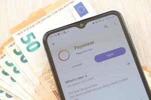 TERNOPIL, UKRAINE - AUGUST 3, 2023 Payoneer application on screen on modern smartphone and many bills of euro currency photo