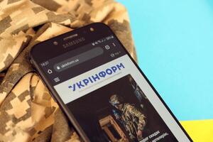 KYIV, UKRAINE - 4 MAY, 2023 Ukrinform ukrainian news portal on smartphone screen with ukrainian flag and camouflage fabric photo