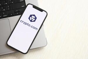 KYIV, UKRAINE - MARCH 15, 2024 Crypto com logo on iPhone display screen on MacBook panel logo on iPhone display screen with dollars and bitcoins on MacBook photo