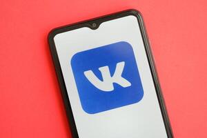 KYIV, UKRAINE - APRIL 1, 2024 Vkontakte icon on smartphone screen on red table photo
