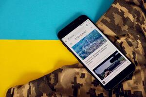 KYIV, UKRAINE - 4 MAY, 2023 Zaxid Net ukrainian news portal on smartphone screen with ukrainian flag and camouflage fabric photo