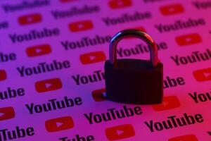 KYIV, UKRAINE - NOVEMBER 27, 2023 Locked small lock on many Youtube logotypes in red and blue light photo