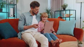 Child kid daughter having fun with father or nanny enjoying using digital tablet play game at home video