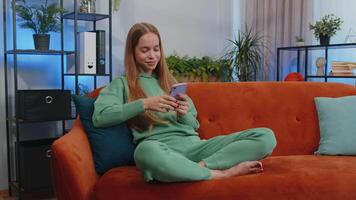 Portrait of teen girl sitting on sofa, using smartphone share messages on social media application video