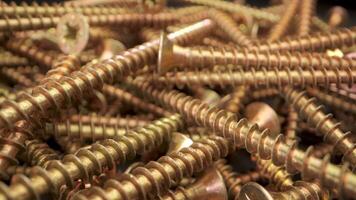 Close up view of a pile of gold screws. The screws are arranged in a random pattern and are illuminated by a bright light. The captures details of the screws, including the threads and the heads video
