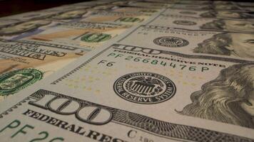 A close-up shot of a stack of one hundred dollar bills, showing the portrait of Benjamin Franklin and the details of the currency. Moving camera video