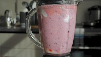 On the countertop there is a picture of a blender with a pink smoothie inside. The smoothie is made from berries and milk. video