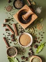 Various dry spices in small bowls and scattered on green background photo
