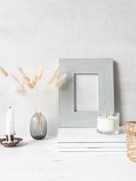 Modern still life of white dry lagurus flower in glass vase and various items on stack of white magazines photo