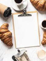 Flat lay frame of cups of coffee, croissants and clipboard with blank sheet for menu photo