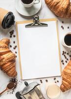 Flat lay frame of cups of coffee, croissants and clipboard with blank sheet for menu photo
