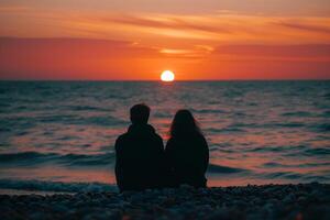 Couple silhouetted against orange sunset over ocean photo