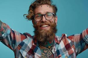 Smiling bearded man with tattoos wearing glasses and plaid shirt against blue background photo