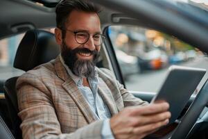 Happy bearded man using tablet while driving car in city photo