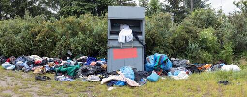 Clothing Donation Overflow. Overflowing donation bin with scattered clothes in a natural setting. photo