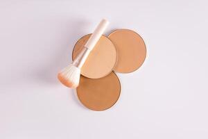 A top view of three blocks of compact powder in different tones and a delicate brush for makeup. white background. Layout for product presentation. photo